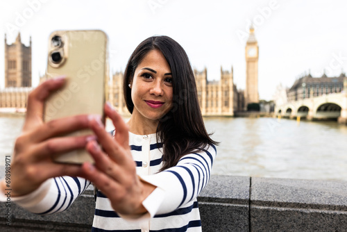 Smiling woman taking selfie with Big Ben and Houses of Parliament through smart phone in London city photo