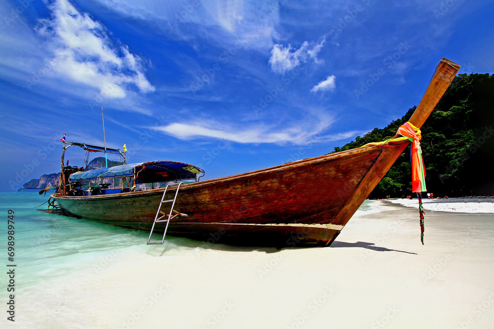 Big long tail boat parking on the white sand beach with blue sky and white clouds at Phi Phi island Krabi, Thailand.