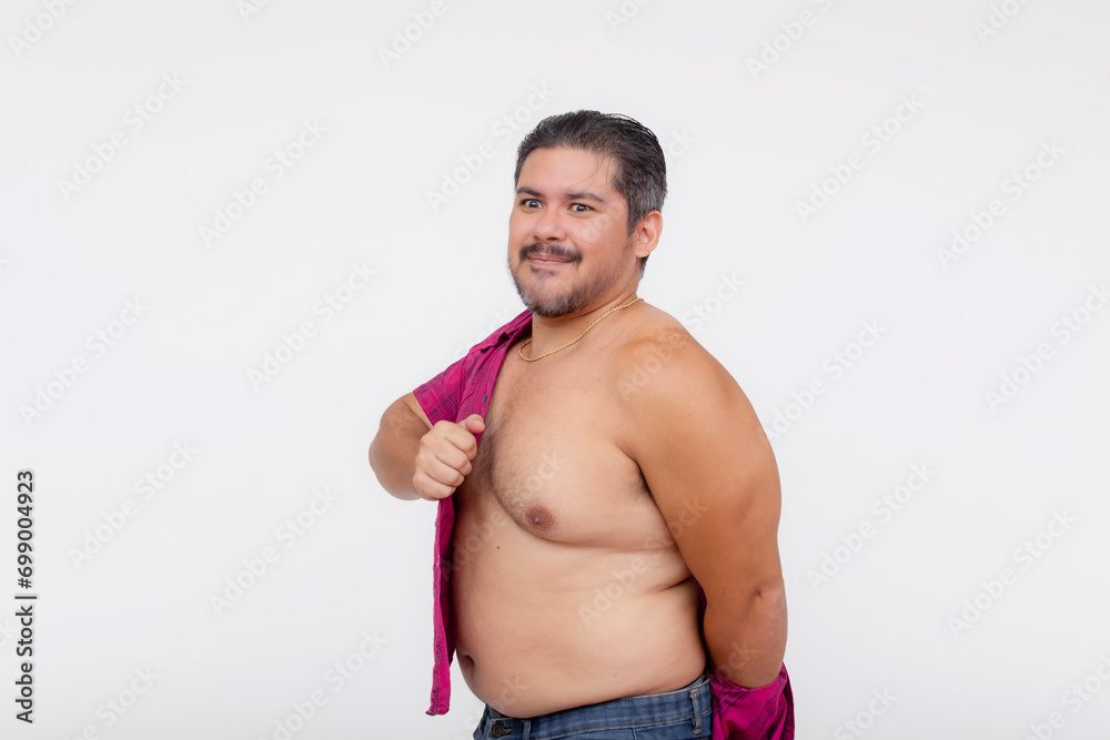 An overweight man struggles to put on an undersized polo shirt that used to fit him. A shirt too small or consequence of gaining too much weight. Isolated on a white background.