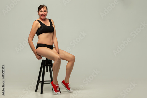 Attractive older woman 50 years old wearing stylish black underwear isolated on gray background.