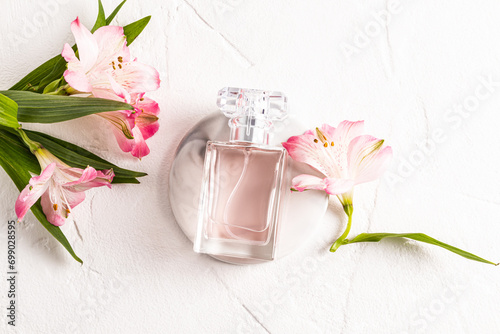 A chic bottle of women's perfume lies on a round marble podium and a white background with delicate astromeria flowers. Top view. Empty bottle. photo