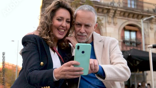 Cheerful mid adult couple having fun together taking a selfie in the street. Romantic senior couple smiling taking picture together in european city. photo