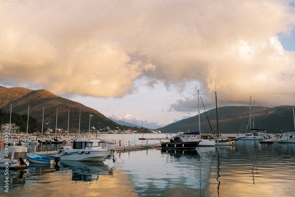 Marina with yachts at the foot of the mountains against the backdrop of orange clouds in the reflections of the sunset