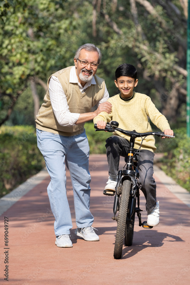 Boy learning bicycle with assistance of grandfather at park Boy learning bicycle with assistance of grandfather at park
