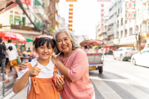 Happy Asian family grandmother and grandchild girl walking and shopping together at street market. Senior woman and little girl enjoy and fun outdoor lifestyle travel in the city on summer vacation. photo