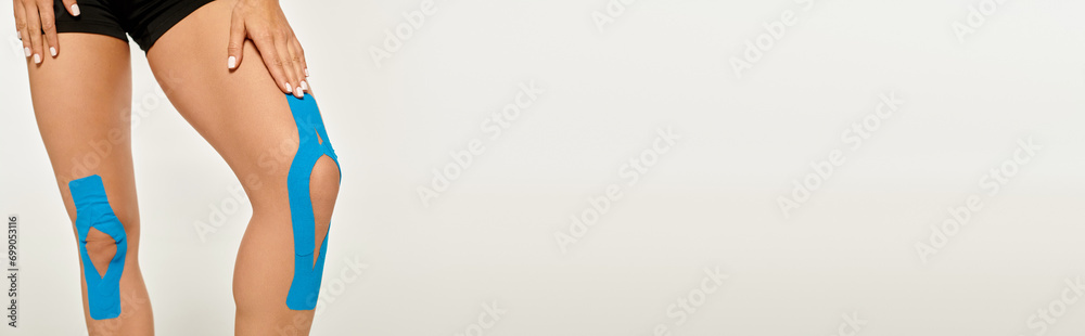cropped view of young woman with kinesiological tapes on her knees on gray backdrop, banner - obrazy, fototapety, plakaty 