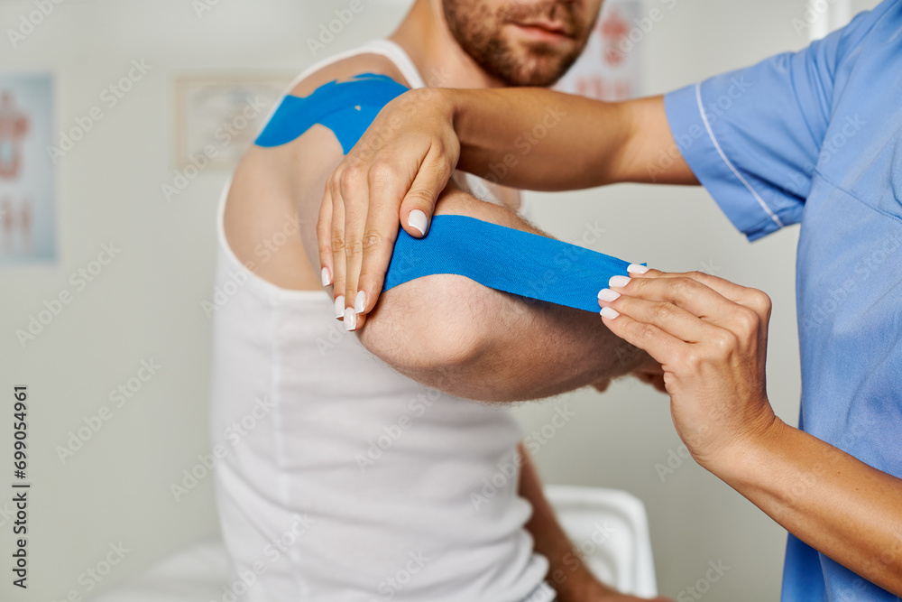Obraz premium cropped view of female doctor putting kinesio tape on elbow of her bearded patient, healthcare