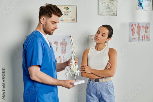 attractive female patient looking at ner handsome bearded doctor with spine model in his hands photo