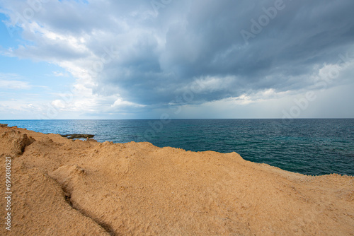 Looking at the sea from the coastal green area. Looking at the sea from the rocks on a cloudy day. Sea view from red cliffs.Cyprus coast.