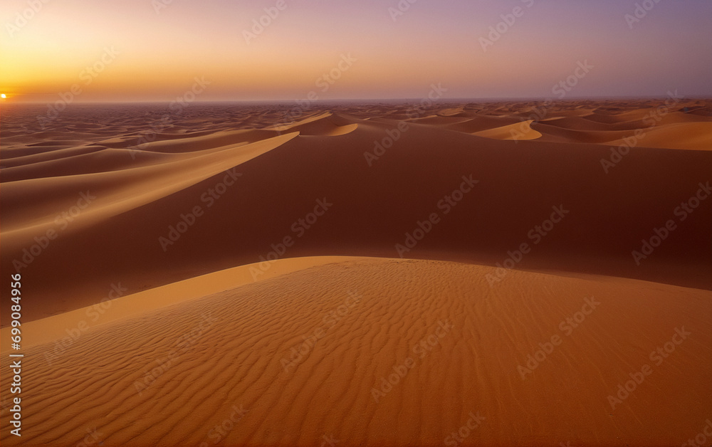Sunset over a desert with sand dunes and purple-yellow sky.