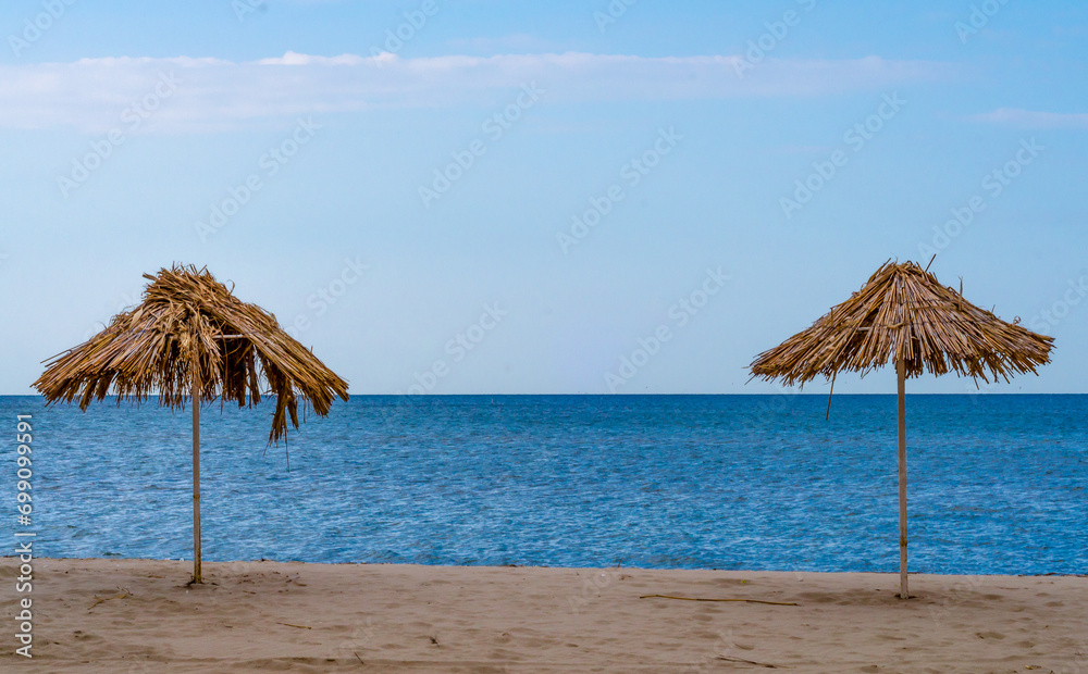 two straw beach umbrellas on an empty seashore on a clear day