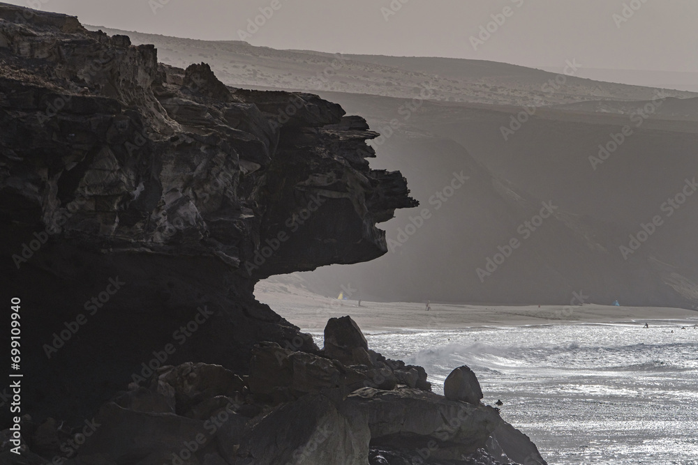 Φωτογραφία View of the silhouettes of rocks, the ocean and the figure of a fisherman in the distance on the beach La Pared on the Canary island of Fuerteventura, Spain