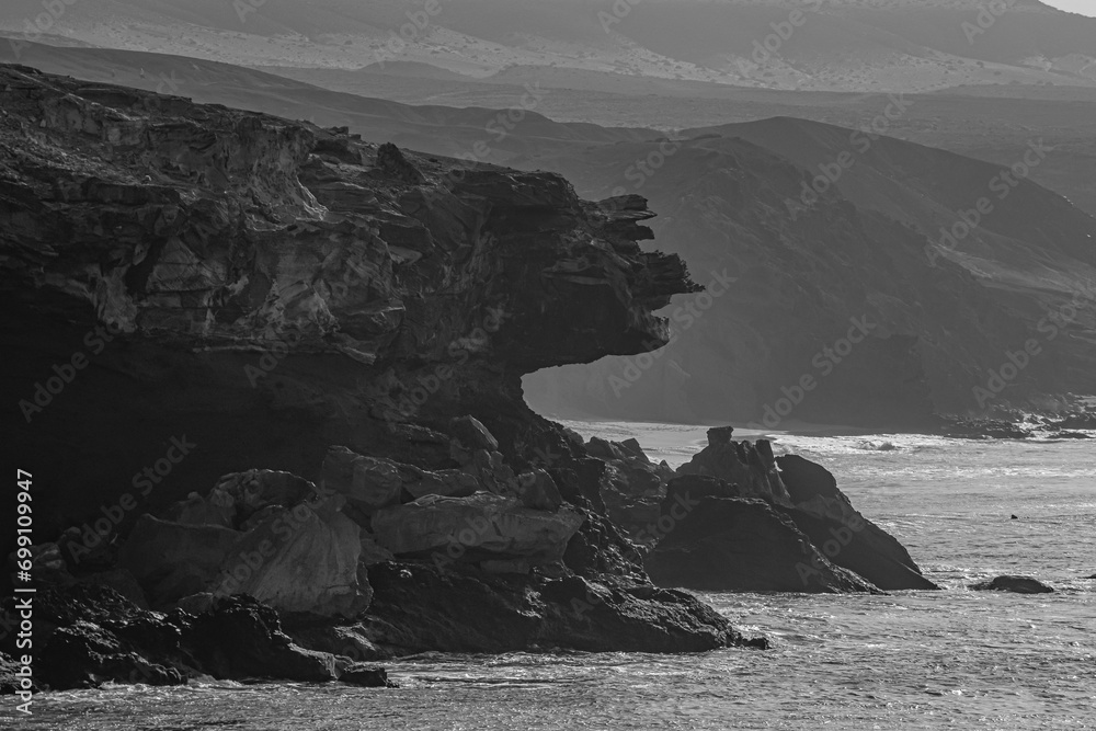 Φωτογραφία View of the silhouettes of rocks, the ocean and the figure of a fisherman in the distance on the beach La Pared on the Canary island of Fuerteventura, Spain