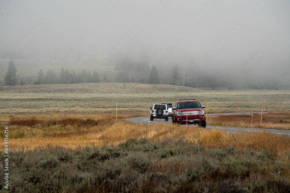 Fototapeta premium Car driving in North american endless asphalt mountain road in autumn, Yellowstone National Park, Wyoming, USA 