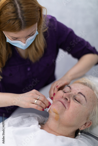 A beautician dressed in a purple uniform cleanses the client's face.