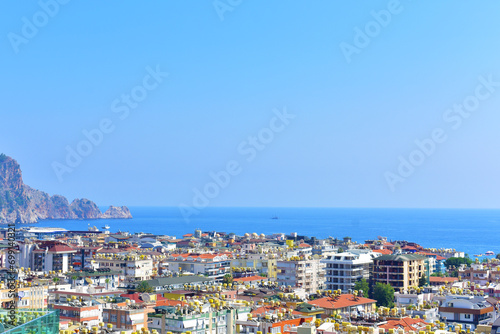 City view with multi-storey modern cottages, blue calm sea and mountain on a summer day. Turkey, Alanya, July 2023.