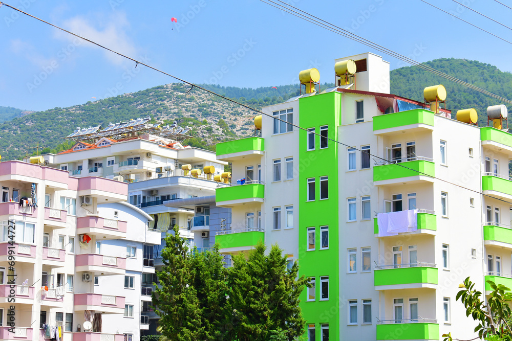 Modern residential house with white and green walls, balconies, trees and mountain against a blue sky background. Sunny summer day. Citylife. Human life. Alanya, Turkey, July 2023 Modern residential house with white and green walls, balconies, trees and mountain against a blue sky background. Sunny summer day. Citylife. Human life. Alanya, Turkey, July 2023