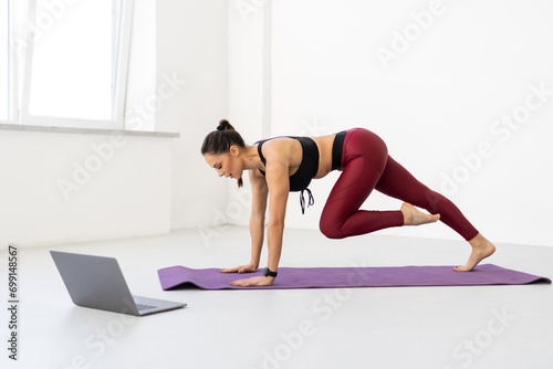 Young woman exercising in front of laptop, watching fitness video on Internet or having online fitness class