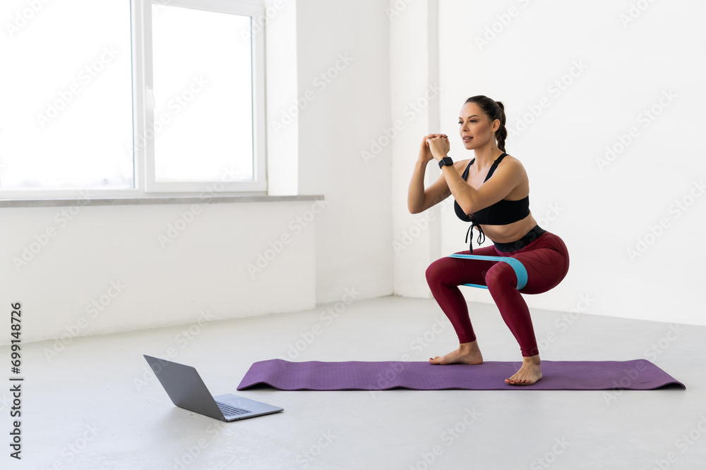 Young woman with resistance band in the morning at home and using online lesson on laptop Young woman with resistance band in the morning at home and using online lesson on laptop