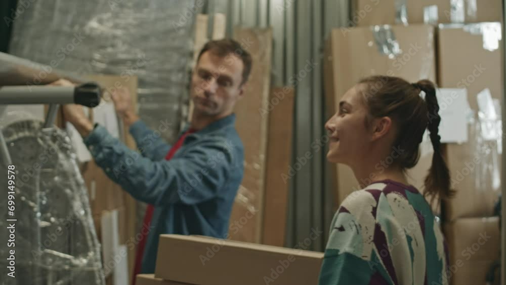 Following shot of young woman carrying cardboard boxes into self storage unit while helping husband with leaving belongings before relocation
