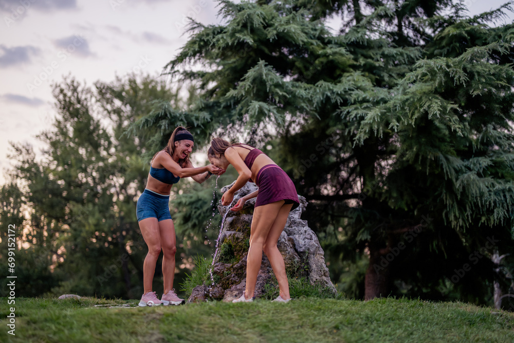 Fit and flexible females having fun outdoors, playing and splashing water in a park fountain after strenuous training. Embracing a healthy lifestyle with happy and active smiles. Fit and flexible females having fun outdoors, playing and splashing water in a park fountain after strenuous training. Embracing a healthy lifestyle with happy and active smiles.