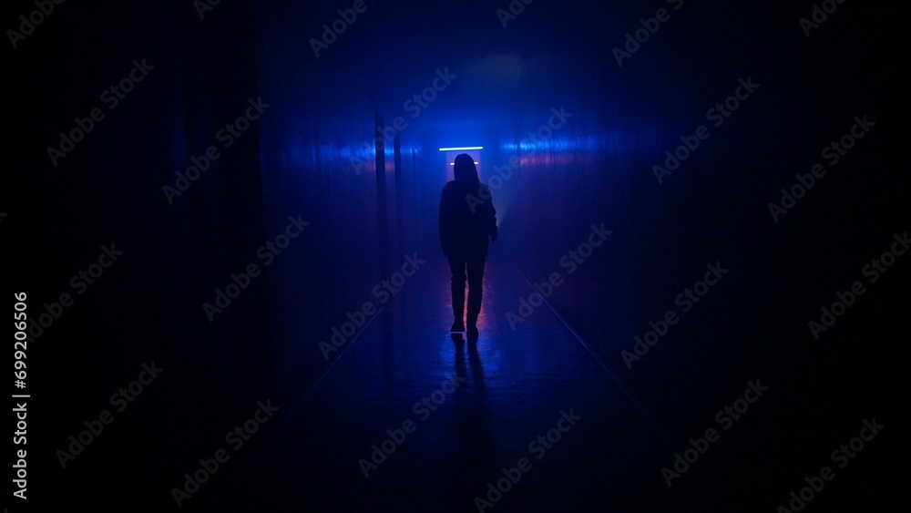 Portrait of female in the dark hallway with neon light. Woman with flashlight walking down the corridor with door and staircase.