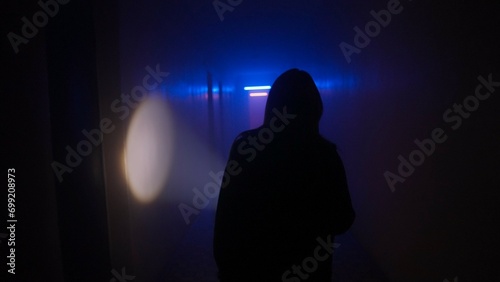 Portrait of female in the dark hallway with neon light. Woman with flashlight facing the camera walking down alone in the corridor. © kinomaster