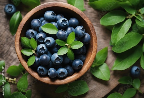 Top view from fresh Vaccinium myrtillus European blueberry and green leaves in a wooden bowl photo