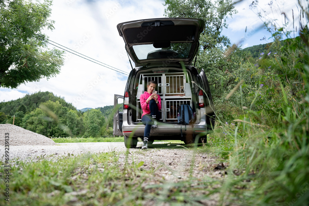 Young woman on a roadtrip with her dogs resting as she sits in an open trunk of her car