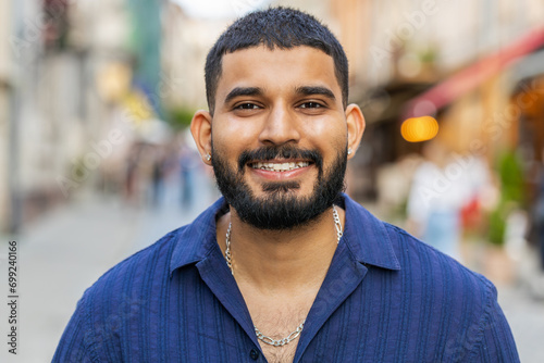 Portrait of happy bearded indian man smiling friendly, glad expression looking at camera dreaming, resting, relaxation feel satisfied good news outdoors. Guy in urban city sunshine street background