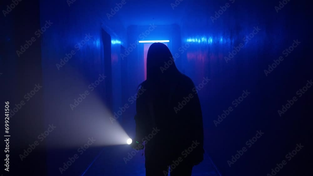 Portrait of female in the dark hallway with neon light. Close shot woman with flashlight facing camera walking down the corridor. Portrait of female in the dark hallway with neon light. Close shot woman with flashlight facing camera walking down the corridor.