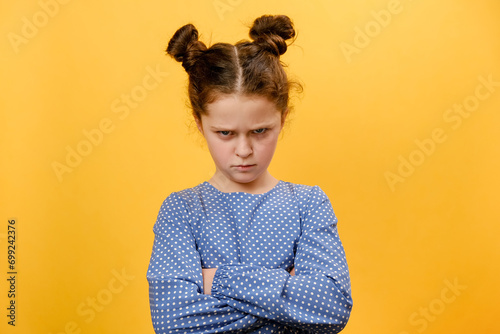 Portrait of grumpy preteen girl child pouting lips, grimacing and looking angrily at camera, posing isolated over plain yellow color background wall in studio. People emotion lifestyle concept