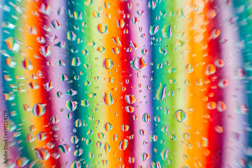 Water droplets on a glass surface with a blurred background showcasing a spectrum of colors in vertical lines photo