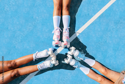 Crop young girlfriends with roller skate legs meeting together on sports ground