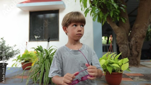 Preschool boy stands on street on summer day, takes out sunglasses from his pocket and puts them on. 