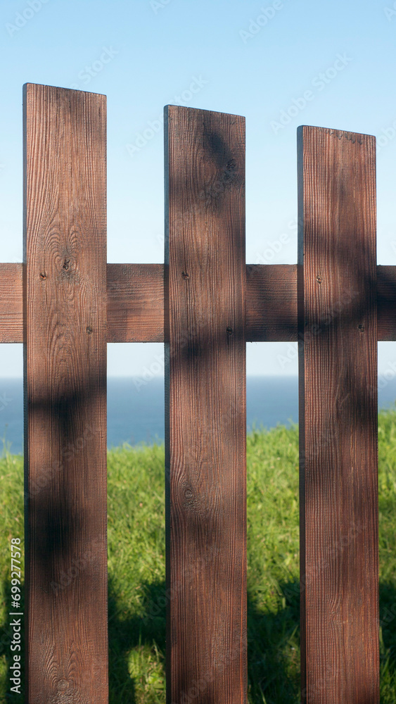 Valla de piquetes de madera en prado de hierba junto al horizonte marino