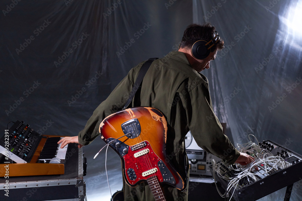 back-view-of-male-sound-producer-with-scuffed-electric-guitar-behind