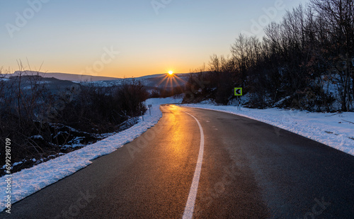 Empty asphalt road in rural landscape at sunset. Blue sky above the road. The sun s rays fall on the wet asphalt of the main road. Winter scene.