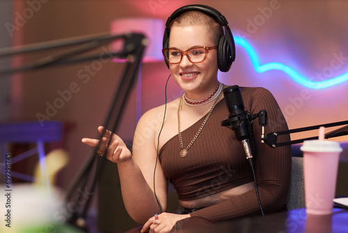 Medium shot of cheerful female blogger wearing headphones talking with guest while recording podcast in studio
