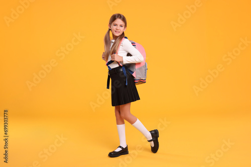 Happy schoolgirl with backpack on orange background photo
