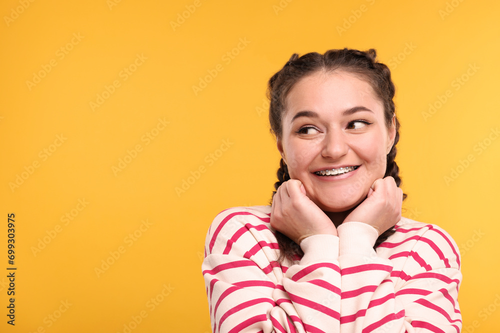 Smiling woman with braces on orange background. Space for text - obrazy, fototapety, plakaty 