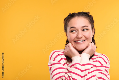 Smiling woman with braces on orange background. Space for text photo