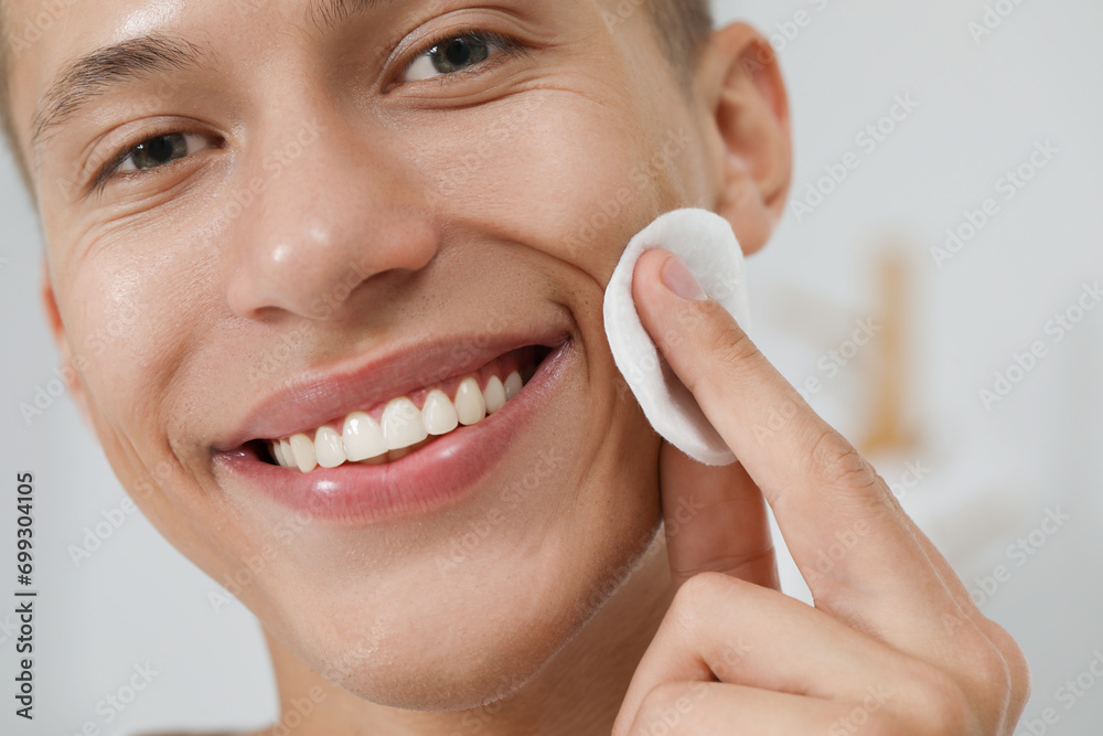 © New Africa - Handsome man cleaning face with cotton pad against blurred background, closeup © New Africa - Handsome man cleaning face with cotton pad against blurred background, closeup