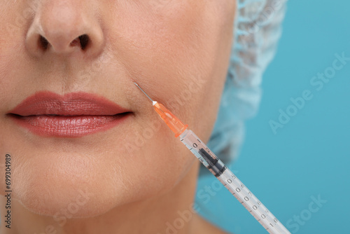 Senior woman getting facial injection on light blue background, closeup. Cosmetic surgery