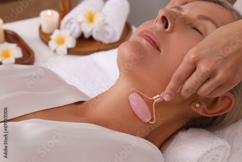 Woman receiving facial massage with rose quartz roller in beauty salon, closeup