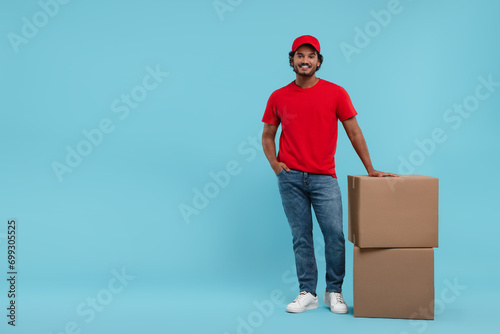 Happy courier with parcels on light blue background, space for text photo