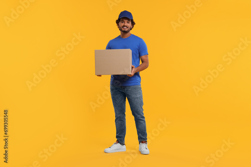 Happy young courier with parcel on orange background