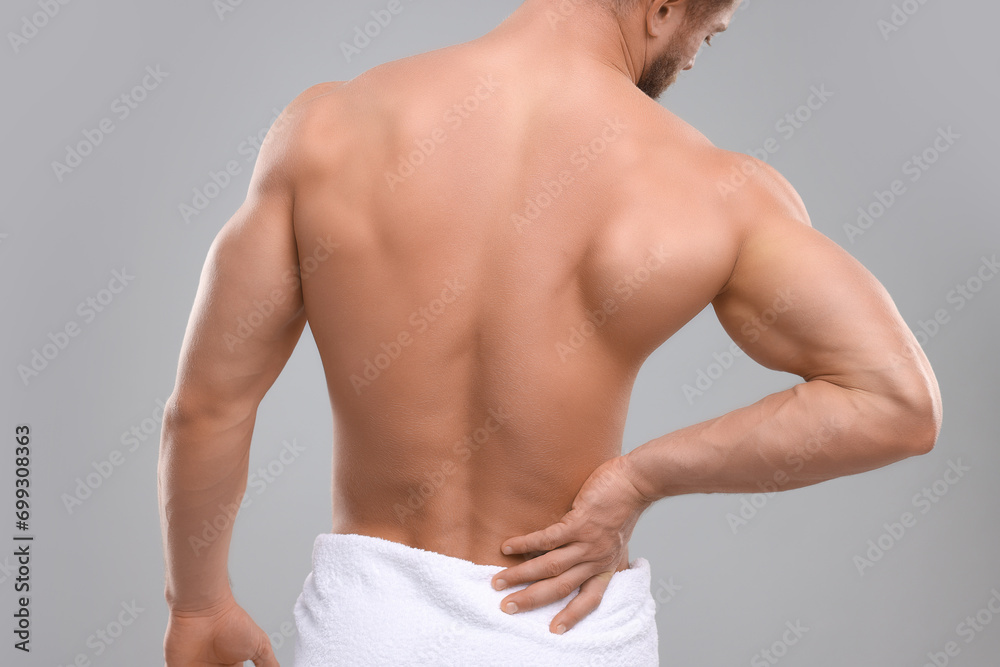 Man suffering from back pain on grey background, back view