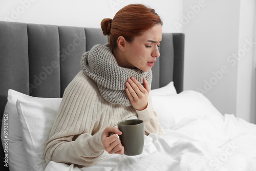 Woman with cup of drink and tissue coughing at home, space for text. Cold symptoms