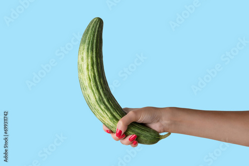 Women hand holding cucumber like a man's penis on blue background. Erotic concept.